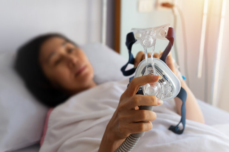 Obstructive sleep apnea therapy..Senior patient woman hands holding Cpap mask lying in hospital room,selective focused.
