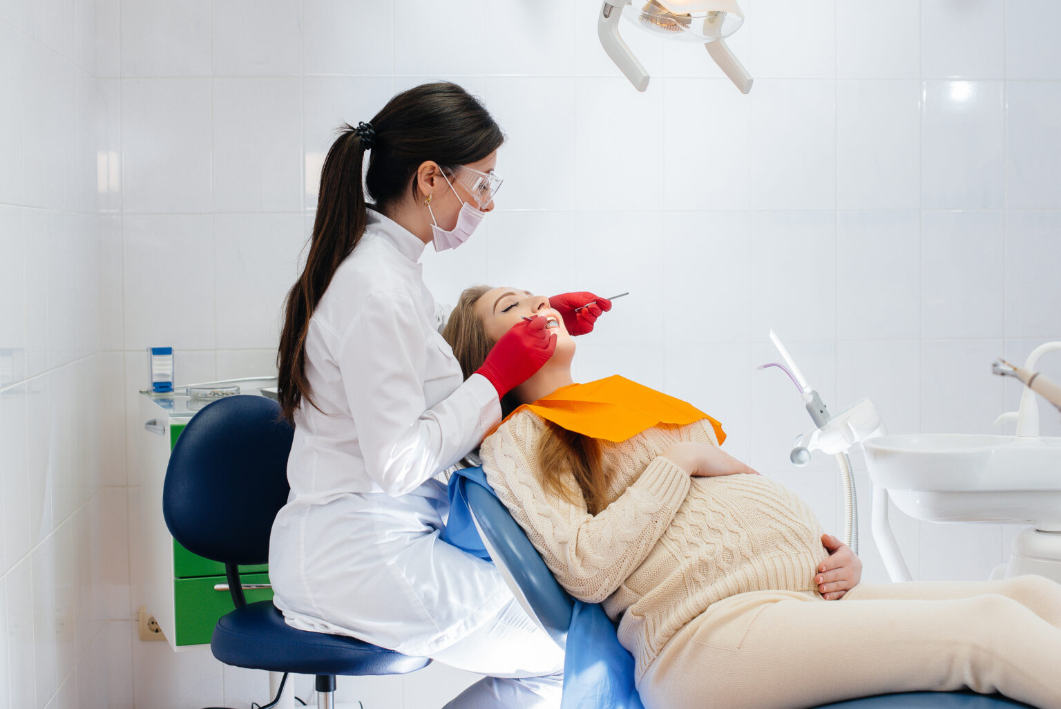 A professional dentist treats and examines the oral cavity of a pregnant girl in a modern dental office. Dentistry