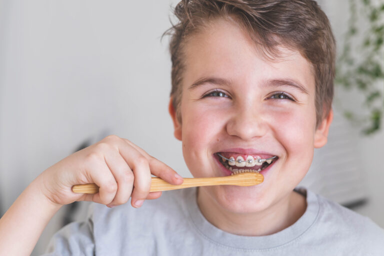 Happy boy child cleaning teeth with braces use wooden eco friendly toothbrush enjoy healthy lifestyle. Portrait overjoyed smiling male kid dental hygiene mouth stomatology toothpaste brushing closeup